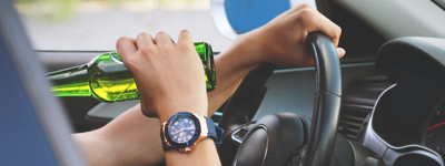 Person holding beer in hand while driving car.